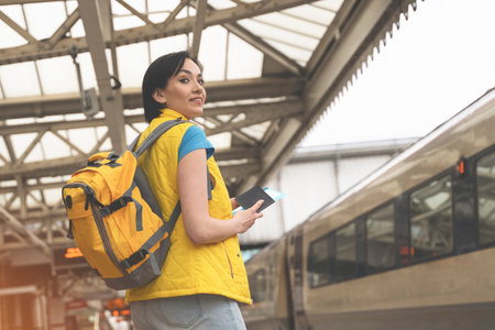 cheerful young woman with backpack passport tickets waiting for train at railway station Enjoying vacation conceptの写真素材