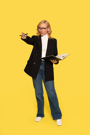 serious woman with pen and folder pointing with index finger on yellow backgroundの写真素材
