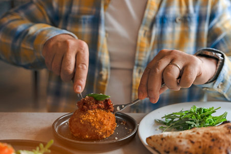 person using fork to eat fried arancini ball topped with tomato sauce and basil.の写真素材
