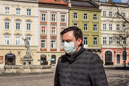 LVIV,UKRAINE, 22 March 2020: handsome young European man on the empty street wearing disposable protective face mask during epidemic of Covid-19のeditorial素材
