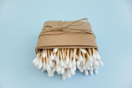 Bamboo cotton sticks or swabs in paper box bound with flax or hemp cord on blue background. Copy...