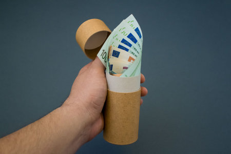 Man's hand holding recycled paper tube with euro money banknotes. Recycling packaging and saving...