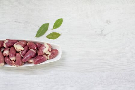 Top view on raw chicken hearts in blue bowl with aromatic spices, bay leaves and peppercorns, on white wooden background with copy spaceの写真素材