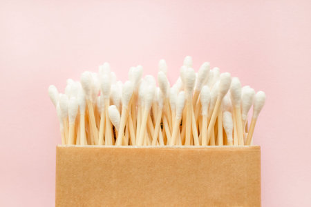 Close up of bamboo cotton sticks in paper box on pink background. Copy space for your design, zero...