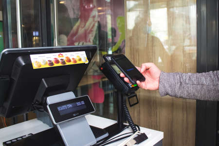 Lviv, Ukraine - May 17, 2020 : McDonalds restaurant, customer is paying with smartphone using NFC technology contactlessly. Contactless and social distance concept, reopening businessのeditorial素材