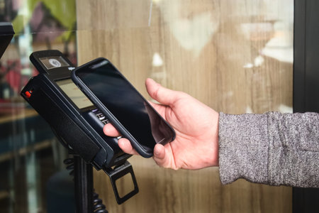 Lviv, Ukraine - May 17, 2020 : close up of customer is paying with smartphone using NFC technology contactlessly. Contactless and social distance concept, reopening businessのeditorial素材