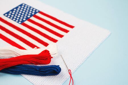 Cross stitch american flag with threads and needle on light blue background. National symbolic of USA - flag Old Glory. Flag Day and Independence Day celebration concept, handmade patternの写真素材