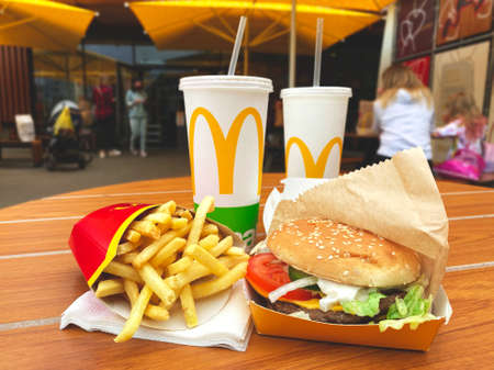 Lviv, Ukraine - June 15, 2020 : tasty lunch at McDonald's restaurant on wooden table - delicious burger with fresh vegetables, french fries, two paper cups with coca cola. New seasonal summer menuのeditorial素材