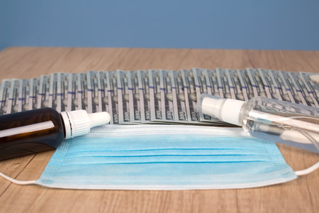Disposable face mask, sanitizer and vaccine or medicine with paper money banknotes as background...