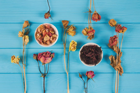 Flat lay with dry rosebuds, hibiscus petals for preparing karkade tea and homemade face, body masks and toners on blue wooden background. Alternative medicine or home spa beauty treatments conceptの写真素材