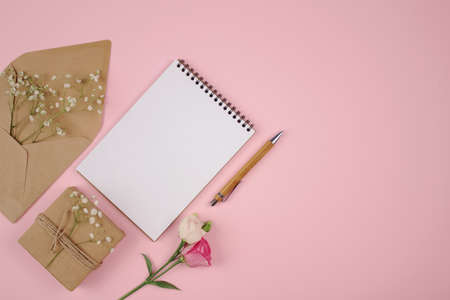 Beautiful holiday flat lay composition with wooden pen, copybook, presents boxes and kraft paper envelope on pastel pink background with copyspace. Holiday shopping list or bridal list concept. Mockupの写真素材