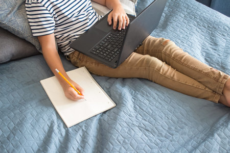 Top view on boy writing or drawing and using his laptop while doing homework. Studying online during...