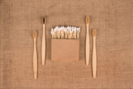 Cotton buds in kraft paper box and natural bamboo toothbrushes on natural burlap background - zero...