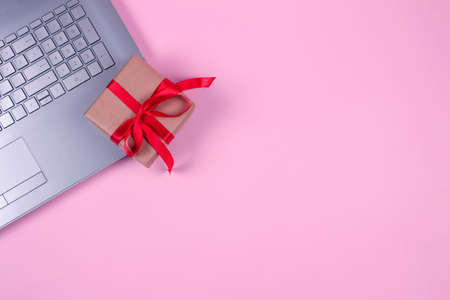 Top view on laptop computer with present box bounded with red tape on pastel pink background with copyspace for your text. Seasonal sale, black friday and cyber monday concept, online shoppingの写真素材