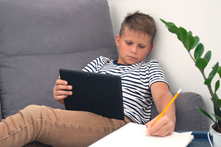 Portrait of diligent boy on self isolation, using his laptop while doing homework. Distance or home...