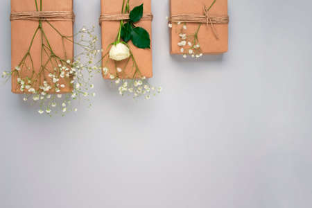 Beautiful flat lay composition with gifts or presents boxes, wraped with kraft paper and white flowers - on light grey background with copyspace. Birthday or Christmas presents conceptの写真素材
