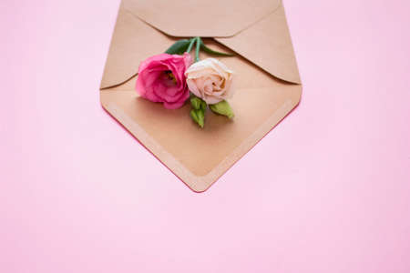 Roses in paper kraft envelope on pastel pink background - festive and vintage floral composition with copyspace. Holidays, wedding celebration, birthday greetings concept. Leaflet or invitation flyerの写真素材
