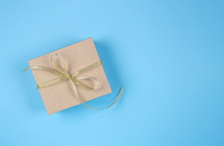 Gift box with golden bow on pastel blue background with copyspace for your text. Flat lay style....