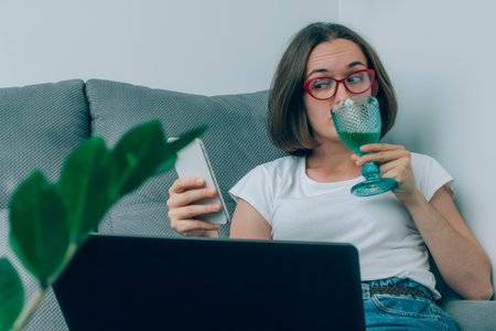 Young woman or freelancer holding a glass of wine, working remotely from home using laptop. WFH and stress at work concept, burnout symptoms. Selective focusの写真素材