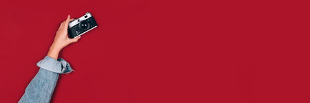 Banner with female hand holding old retro photo camera on red background with copy space for text. Trendy vintage photography. Online photography school concept, selective focusの写真素材
