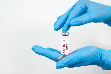 Female scientist or doctor hands holding vial dose of COVID-19 vaccine with syringe against white background with copy space - prevention coronavirus, global vaccination concept. Selective focusの写真素材