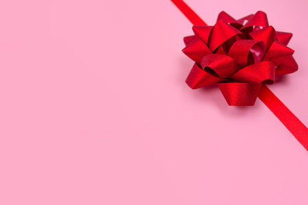 Decorative red ribbon bow on pink background with copy space for text. Giving presents concept. Greeting card or holidays sale background, selective focusの写真素材