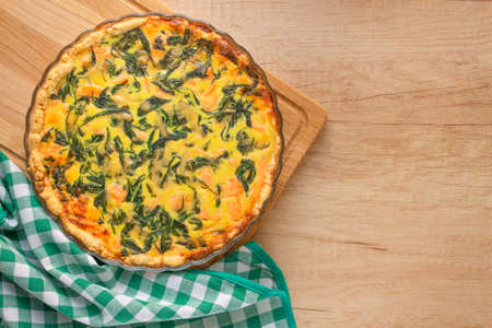 Salty pastries - salmon fish or seafood and spinach leaves quiche pie - homemade recipe pie on wooden table background with copy space, selective focus. Top viewの写真素材