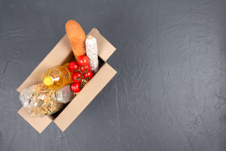 Top view on Easter donation box with different food donations on gray background with copy space - pasta, fresh vegatables, canned food, baguette, cooking oil. Food bank, food delivery conceptの写真素材