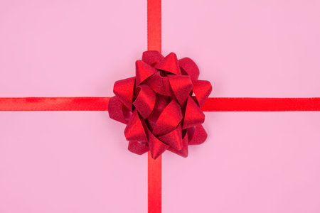 Festive composition with decorative red ribbon bow on pink background with copy space for text....