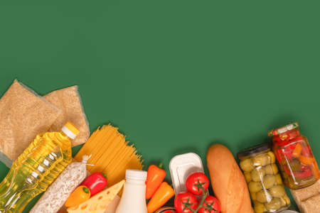Different groceries, food donations on green background with copy space - pasta, vegatables, canned food, baguette, cooking oil, tomatoes, cheese. Food bank or food delivery concept, selective focusの写真素材