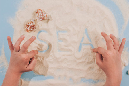 Childs hands playing with sea shells and sand - Montessori education concept. Fine motoric skills or...