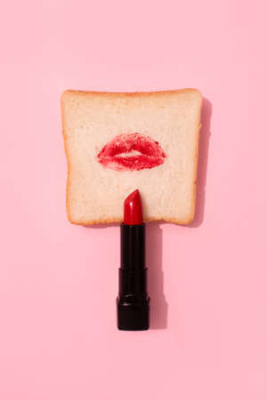 Creative abstract composition with red lipstick and lips on bread on bright pink background. Creative makeup concept. Selective focus, vertical imageの写真素材