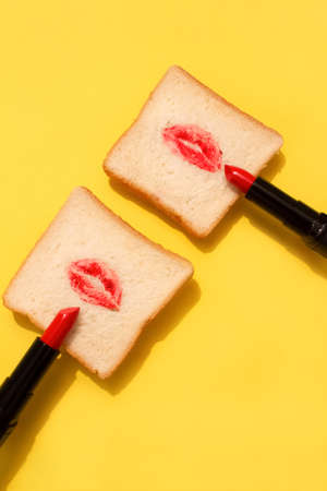 Creative concept made with red lipstick and lips on bread on bright yellow background. Minimal abstract composition. Creative makeup concept. Selective focus, vertical imageの写真素材