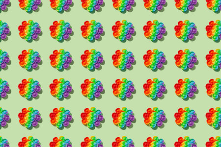 Pattern made with rainbow pop it fidget toy on green background. Push bubble fidget sensory toy -...