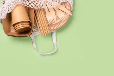 Eco-friendly tableware - kraft paper food cups, plates and containers with wooden cutlery in cotton bag on green background with copy space. Street food paper packaging, sustainable packaging conceptの写真素材