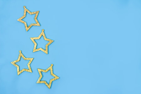 Festive background with golden Christmas ornaments - stars decorations on pastel blue background...