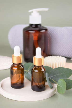 Set of natural beauty treatments - glass dropper bottles with natural organic cosmetics, natural face or body dry brush, eucalyptus oil, cream, lotion, essential oils on green background, mockupの写真素材