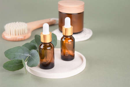 Glass dropper bottles and jars with natural organic cosmetics, natural bristles face or body dry brush - eucalyptus oil, face or body cream, essential oils on green background with copy space, mockupの写真素材