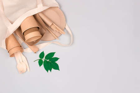 Eco-friendly tableware - kraft paper cups and containers in white cotton bag on light gray background with copy space. Street food take away paper packaging - cups, plates, straws. Selective focusの写真素材