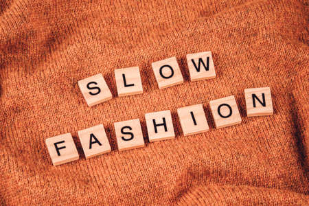 Slow fashion concept. Wooden bricks with letters on orange knitted background. Conscious and environmentally friendly consupmtion - new modern trends in shopping. Zero waste, selective focusの写真素材