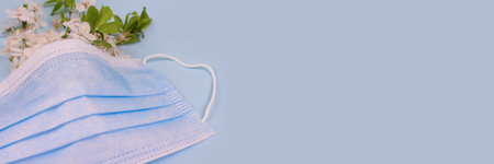 Banner with medical protective face mask and cherry blossom branch on pastel blue background. Seasonal spring allergy concept, selective focus. Copyspaceの写真素材