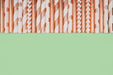 Background made with striped paper drinking straws in golden color on green backdrop with copyspace. Biodegradable and eco-friendly drinking straws for summer cocktails. Selective focusの写真素材