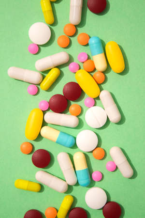 Vertical image of assorted multicolored medicine pills, capsules and tablets on green background. Immune system vitamins and supplemets. Various dietary bio supplements. Selective focusの写真素材
