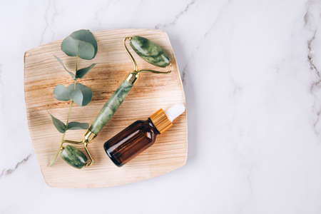 Flat lay composition with jade gua sha facial roller with beauty serum oil on white marble table background with copy space. Facial massage kit - for lifting massage therapy made from natural stonesの写真素材