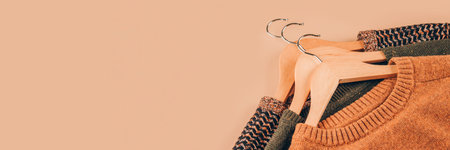 Banner with wooden hangers with sweaters on beige background with copy space. Clothing donations, conscious and environmentally friendly consupmtion - new trends in shopping, slow fashion conceptの写真素材