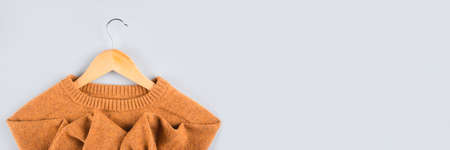 Banner with wooden hangers with orange sweater on gray background with copy space. Clothing donations, conscious and environmentally friendly consupmtion - new trends in shopping, slow fashion conceptの写真素材
