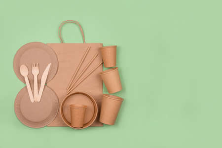 Banner with set of different eco-friendly tableware, kraft paper food packaging and paper bag on green background with copy space. Street food paper packaging - cups, plates, drinking straws. Flat layの写真素材