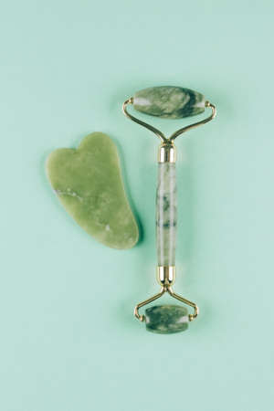 Vertical image - jade facial roller and gua sha tool on pastel green background. Facial massage kit for lifting massage therapy made from natural stones, personal skin care anti-aging toolsの写真素材