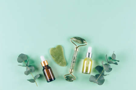 Flat lay composition with jade gua sha facial roller with beauty serum oil on pastel green background with copy space. Facial massage kit - for lifting massage therapy made from natural stonesの写真素材