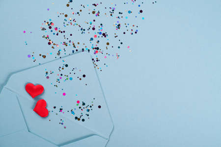 Valentine's day festive background. Blue envelope with red hearts and multicolored confetti around on pastel blue background with copy space. Flat lay, top view. Greeting cardの写真素材